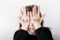 Young woman is covering her eyes with her palms. Eyes painted on her hand.