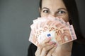 Young woman covering her face with fan of euro money over grey background Royalty Free Stock Photo