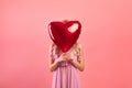 Young woman covering her face with heart shaped balloon on pink studio background. Valentine& x27;s Day concept Royalty Free Stock Photo