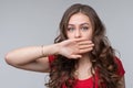 Young woman covering mouth with hand, looking serious, promises to keep secret. Silence and secret concept
