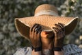 Young woman covers her face with a straw hat. Her hands in black vintage lace gloves. Spring blossom apple tree garden. Royalty Free Stock Photo