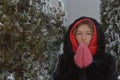 Young woman in a cozy fur coat with a hood and pink mittens on the street in winter. Portrait of a girl dressed in winter clothes Royalty Free Stock Photo