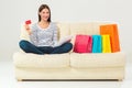 Young woman with credit card buying sitting on sofa with paper bags and new clothes