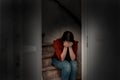 Young woman cries and sitting on a stairs in the dark, lonely sad and depressed girl holding her head down