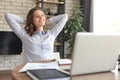 Young woman crossed hands behind head, enjoying break time at home. Peaceful carefree business woman resting at table