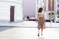 A young woman crosses the road in the city. Beautiful stylish brunette with a bag. Back view Royalty Free Stock Photo