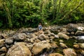 Young woman crossing stream on a trail to Middle Tavoro Waterfalls in Bouma National Heritage Park, Taveuni Island, Fiji