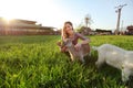 Young woman crouching in spring meadow, feeding small brown goat kid. Wide angle photo with strong sun backlight Royalty Free Stock Photo