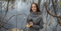 Young woman with a cup of coffee and a bouquet of autumn leaves in the forest near a pond in a fine rain Royalty Free Stock Photo