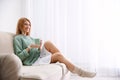 Young woman with cup of drink relaxing on couch near window at home Royalty Free Stock Photo