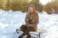 Young woman with cup of hot drink sitting on sled in winter park Royalty Free Stock Photo