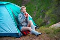 Young woman with a cup of tea near a tent against green forest b Royalty Free Stock Photo