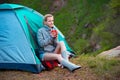 Young woman with a cup of tea near a tent against green forest b Royalty Free Stock Photo