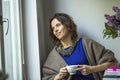 Young woman with cup of tea sitting at a table near the window. Happy. Royalty Free Stock Photo