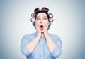 Young woman with curlers opening her mouth holds her hands behind her head, very surprised, scared Royalty Free Stock Photo