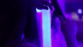 Young woman curling her hair on tongs, doing her hair styling in neon light room