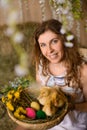 Young woman with curly hair holding basket with ducklings, painted Easter eggs, dandelions Royalty Free Stock Photo