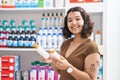 Young woman customer holding sunscreen bottles at pharmacy Royalty Free Stock Photo