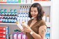 Young woman customer holding sunscreen bottles at pharmacy Royalty Free Stock Photo