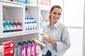 Young woman customer smiling confident holding sunscreen bottles at pharmacy Royalty Free Stock Photo