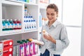Young woman customer smiling confident holding sunscreen bottles at pharmacy Royalty Free Stock Photo