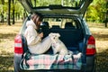 Young woman and cute dog relaxing enjoying happy moment in the forest sitting in car trunk. Royalty Free Stock Photo