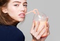 Young woman or cute girl drinking fresh juice or fruit yoghurt from bottle or glass with orange straw, poses on grey Royalty Free Stock Photo