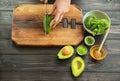 Young woman cutting avocado for nourishing mask at table