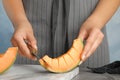 Young woman cutting cantaloupe melon slice at table