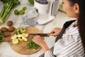 Young woman cutting fresh spinach for juice at table in kitchen Royalty Free Stock Photo