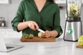 Young woman cutting kiwi for smoothie at white table in kitchen, closeup Royalty Free Stock Photo