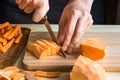 Young woman cutting with knife sweet potato into wedges, peels on wood table, sliced carrots Royalty Free Stock Photo