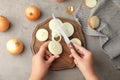 Young woman cutting ripe onion on wooden board at table, top view Royalty Free Stock Photo