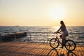 Young woman cycling at the beach at sunrise sky at wooden deck summer time