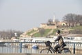 Young woman cycling over city bridge with Kalemegdan fortress in the background