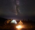 Woman resting at night camping near campfire, tourist tent, bicycle under evening sky full of stars Royalty Free Stock Photo