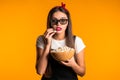 Young woman in 3d glasses watching horror movie and eating popcorn on yellow studio background. Royalty Free Stock Photo