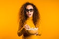 Young woman in 3d glasses watching movie and eating popcorn on yellow background Royalty Free Stock Photo