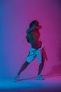 Young woman dancer in stylish youth clothes in gym shoes dancing and posing in a room with bright neon blue-pink color. Sports Royalty Free Stock Photo