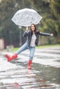 Young woman dances in the rain in the park, holding an umbrella, wearing rainboots