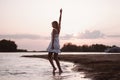 A young woman is dancing on the beach. A beautiful slender happy blonde in a white lace sundress is spinning in the Royalty Free Stock Photo