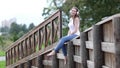 Woman with headphones dangles her legs while sitting on fence in public park.