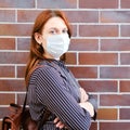 A young woman in dark clothing and medical mask stands near a red brick wall Royalty Free Stock Photo