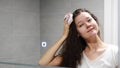 Young woman with dark curly hair doing self hair scalp massage with scalp massager or hair brush for hair growth