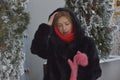 A young woman in a dark fur coat with a hood and pink mittens against the backdrop of snow-covered trees. Portrait of a girl Royalty Free Stock Photo