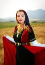 Young woman with dark hair, green and red velvet historical dress and gold jewel and a subtle smile..