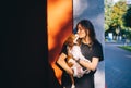 Young woman with dark hair kissing a adorable King Charles spaniel puppyin the city yard