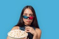 Freestyle. Young woman wearing 3d glasses standing isolated on blue eating popcorn pouting lips concerned close-up Royalty Free Stock Photo