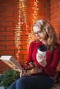 A young woman decorates a house for Christmas and New Year. Holds a box of toys. Against the background of a brick wall