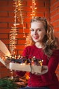 A young woman decorates a house for Christmas and New Year. Holds a box of toys. Against the background of a brick wall